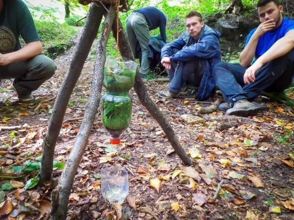 Selbstgebaute Wasserfilterkonstruktion aus Plastikflaschen und Ästen hängt über einem Behälter