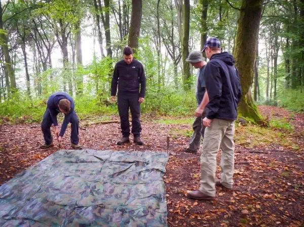 Vier Personen richten eine Tarp-Notunterkunft im Wald aus