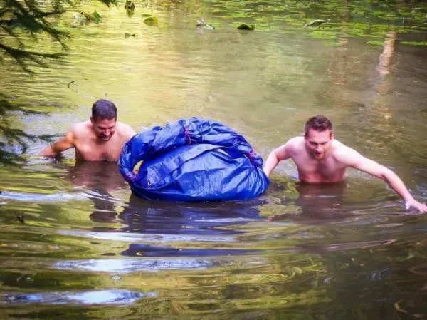 Zwei Männer ziehen einen blauen Sack durch einen Gewässerbereich