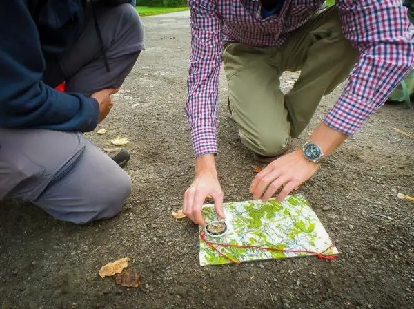 Zwei Personen analysieren eine Karte mit einem Kompass auf dem Boden