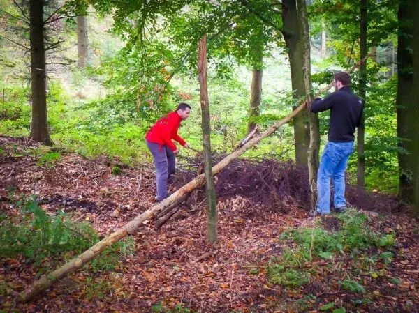 Zwei Personen bauen eine selbstgebaute Konstruktion aus Holzstücken im Wald