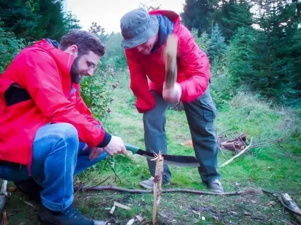 Zwei Personen bearbeiten Holz mit einer Machete beim Survival Training