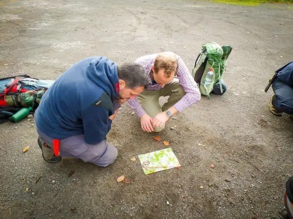 Zwei Personen betrachten eine Karte auf dem Boden, Rucksäcke liegen daneben