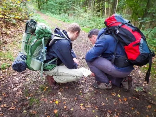 Zwei Personen betrachten eine Karte auf einem Waldweg, Rucksäcke sind sichtbar
