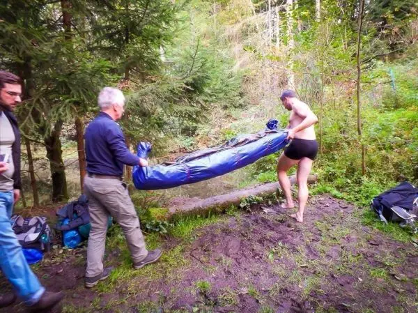 Zwei Personen heben eine blaue Plane am Ufer eines Gewässers