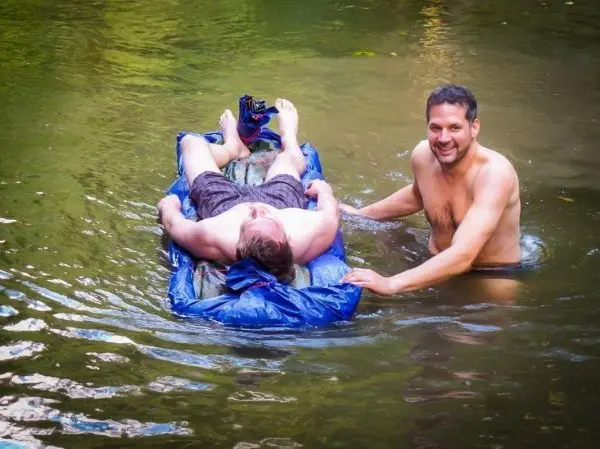 Zwei Personen im Wasser, eine liegt auf einer improvisierten Schwimmhilfe aus blauer Plane