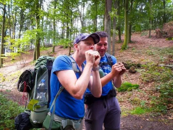 Zwei Personen mit Rucksäcken üben eine Technik im Wald