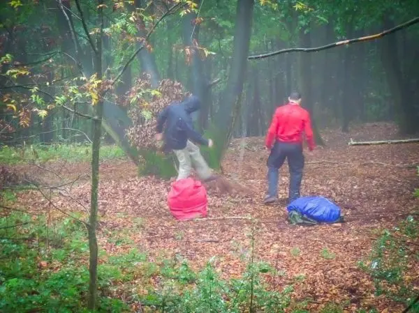 Zwei Personen stehen in einem bewaldeten Gebiet und bearbeiten den Boden