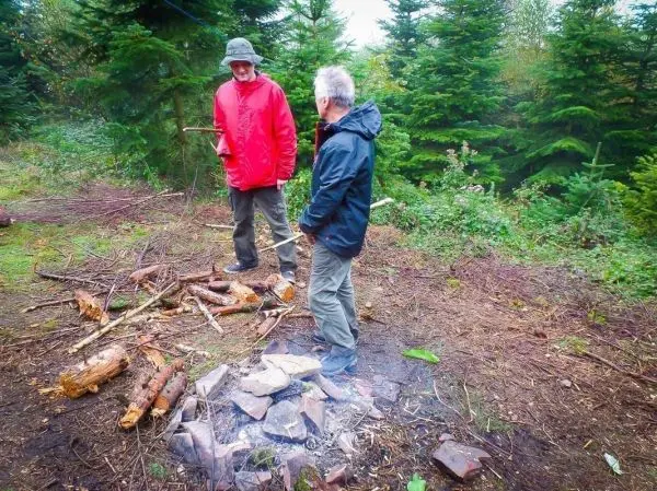 Zwei Personen stehen neben einem Feuerplatz im Wald