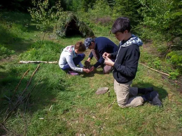 Drei Personen arbeiten am Boden, während eine Tarp-Notunterkunft im Hintergrund sichtbar ist