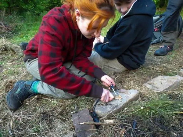 Feuerstahl erzeugt Funken auf Zunder, während eine Person auf dem Boden sitzt