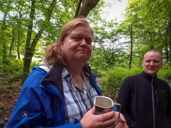 Frau hält einen Metallbecher in einem Waldgebiet