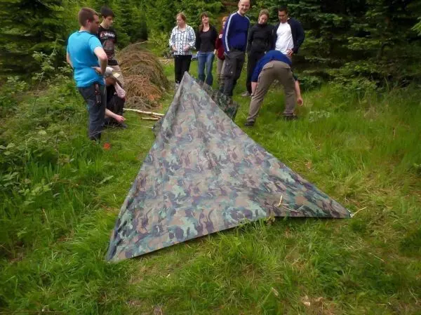 Gruppe baut Tarp-Notunterkunft aus camouflierter Plane und Ästen auf