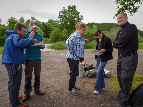 Gruppe betrachtet Kartenmaterial und Ausrüstung auf einem Parkplatz
