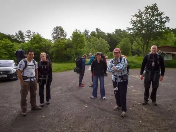 Gruppe mit Rucksäcken steht auf einem Parkplatz umgeben von Bäumen