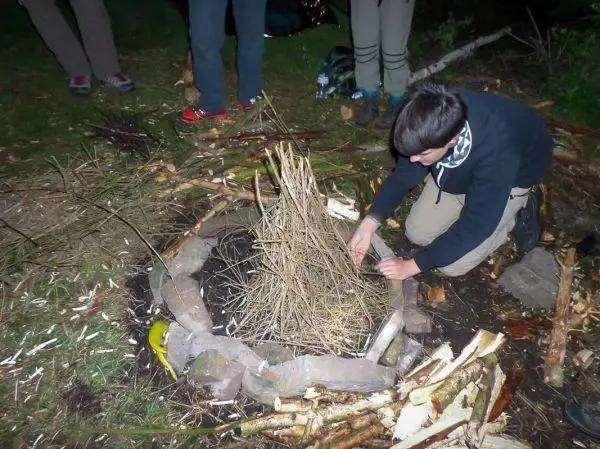 Junge baut Zundernest aus Ästen in einer Feuerstelle aus Steinen