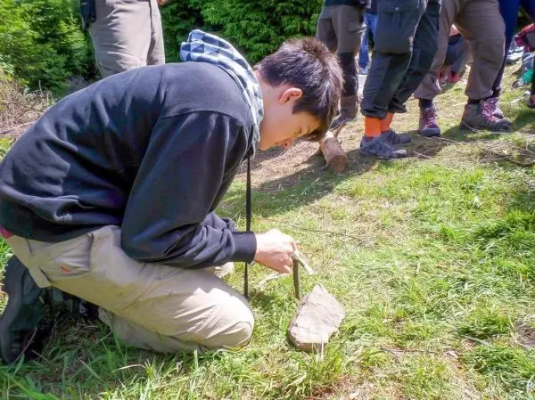 Junge bearbeitet einen Stein mit einem Messer auf dem Boden