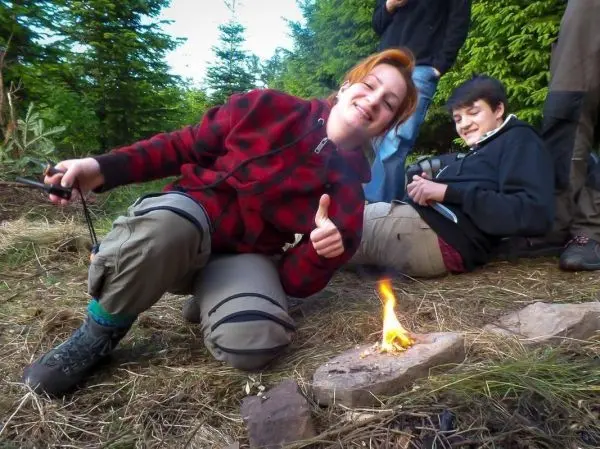 Kleines Bodenfeuer brennt auf einem Stein, während eine Person lächelt und Daumen hoch zeigt