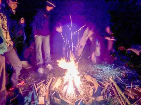 Kleines Bodenfeuer brennt in einer improvisierten Feuerstelle, umgeben von Menschen