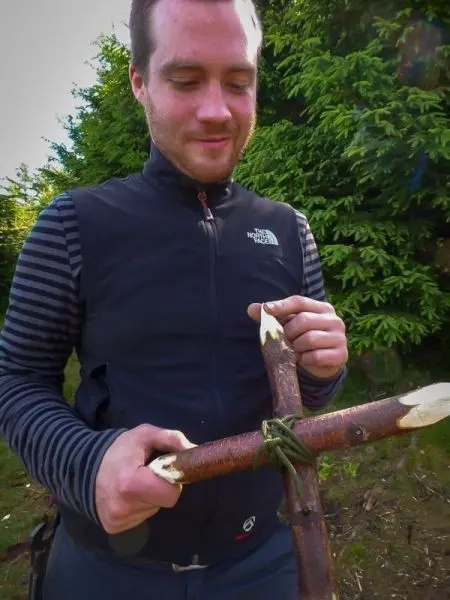 Mann bindet zwei Äste mit Paracord zu einer Kreuzkonstruktion