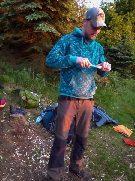 Mann schnitzt mit einem Messer Holzstück in einer natürlichen Umgebung