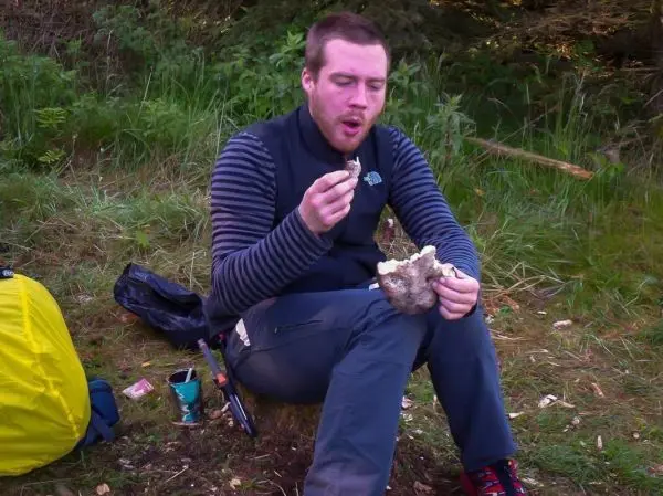 Mann sitzt auf einem Baumstumpf und isst einen Pilz