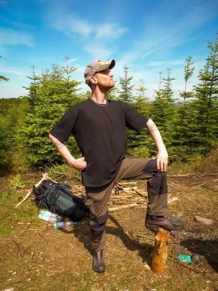 Mann steht auf einem Baumstumpf in der Natur, Rucksack im Hintergrund