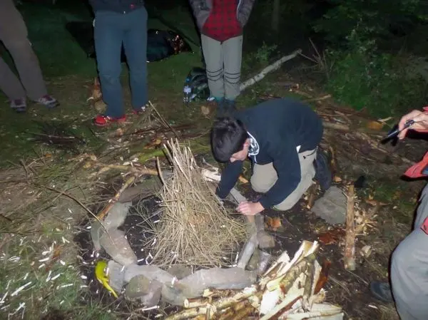 Person baut ein Feuer in einer Steinmulde auf beim Survival Training