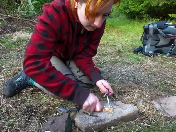 Person bearbeitet Holzstück mit einem Messer im Freien beim Survival Training