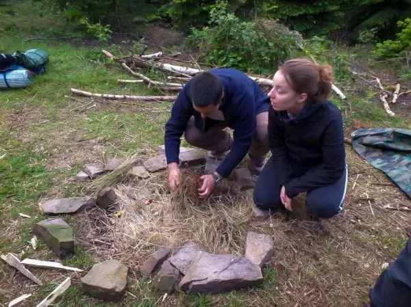 Person bereitet Feuerstelle mit trockenem Gras vor beim Survival Training