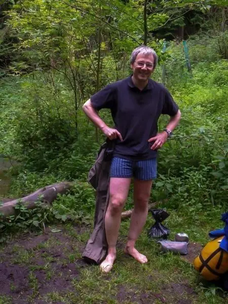 Person zieht Hose an, im Hintergrund grüne Vegetation und ein Baumstamm