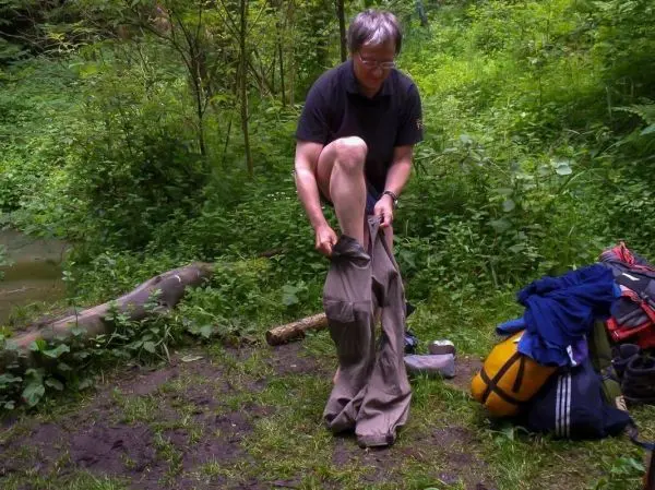 Person zieht Hose an, während Rucksack und Kleidung im Hintergrund liegen