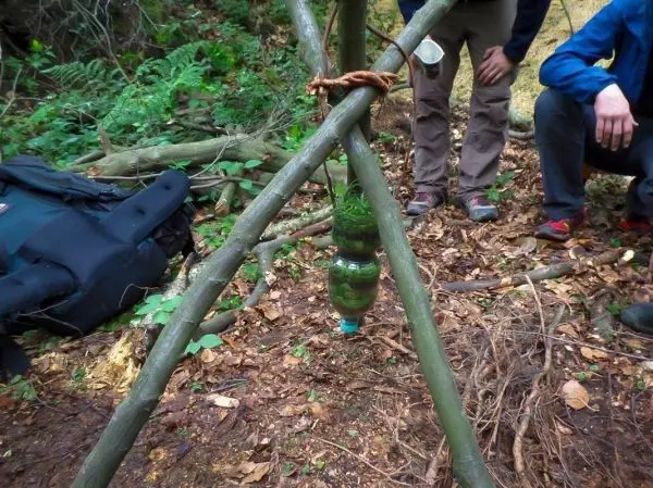 Selbstgebaute Konstruktion mit einer Flasche hängt an einem Dreibein aus Ästen