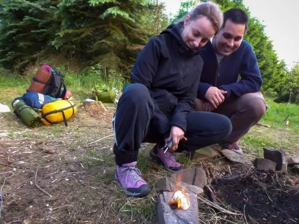 Zunder glimmt auf einem Stein, während zwei Personen aufmerksam zuschauen