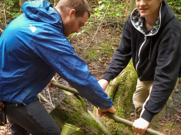 Zwei Personen halten einen langen Stock, um eine selbstgebaute Seilbrücke zu stabilisieren