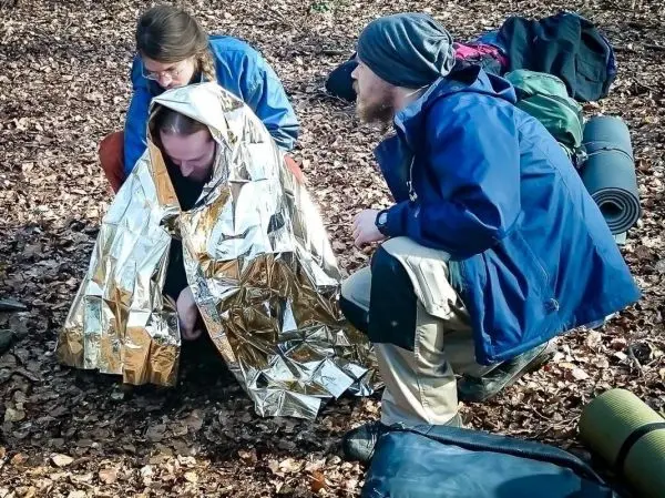 Drei Personen helfen einem Mann, der in eine Rettungsdecke gehüllt ist
