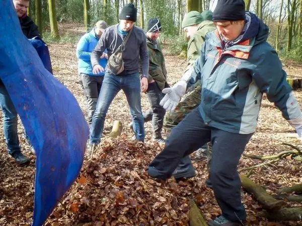 Gruppe arbeitet an einer Tarp-Notunterkunft aus Laub und Ästen im Wald