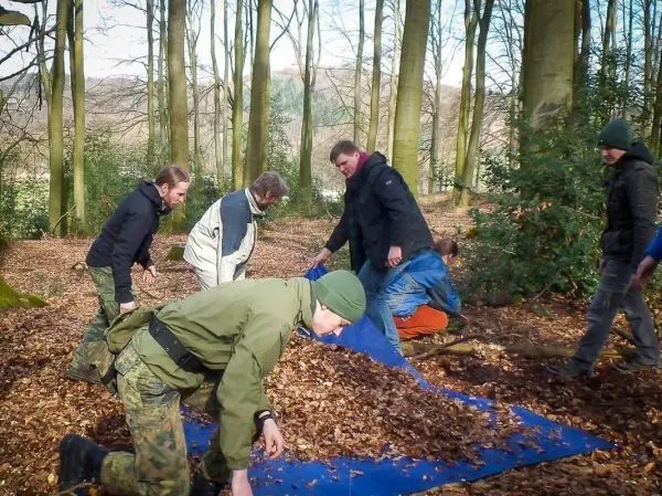 Gruppe arbeitet gemeinsam an einer Tarp-Notunterkunft im Wald