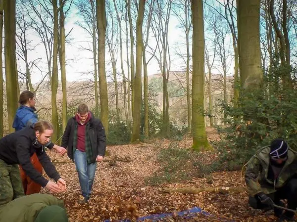 Gruppe arbeitet im Wald an einer Tarp-Notunterkunft auf Laub
