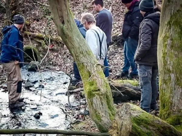 Gruppe betrachtet einen kleinen Bachlauf zwischen Bäumen und Laub