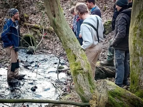 Gruppe steht am Ufer eines kleinen Baches und beobachtet den Boden