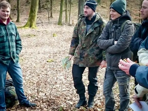 Gruppe von Personen steht im Wald und diskutiert eine Karte beim Survival Training
