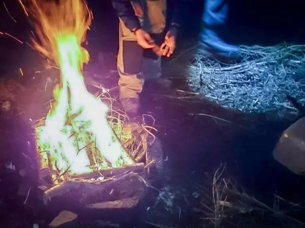 Kleine Flamme brennt in einem Steinkreis, Hände fügen Zunder hinzu