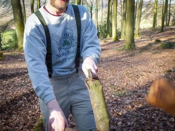 Mann hält einen Holzstock mit einer Handsäge in einem Waldgebiet