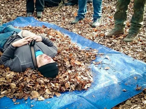 Mann liegt auf einer blauen Plane, umgeben von Laub, mit einem Gurt um den Oberkörper