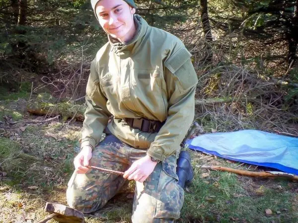 Mann sitzt auf dem Boden und bearbeitet einen Holzstock mit einem Messer