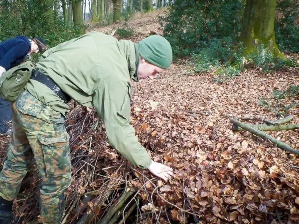 Mann überprüft eine Laubhütte aus Ästen und Blättern im Wald