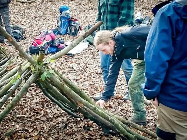 Mann überprüft eine selbstgebaute Notunterkunft aus Ästen im Wald