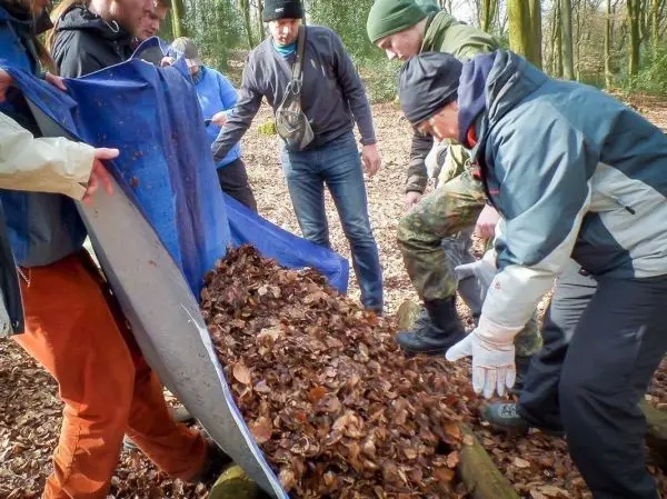 Mehrere Personen kippen Laub aus einer Tarp-Notunterkunft auf den Boden