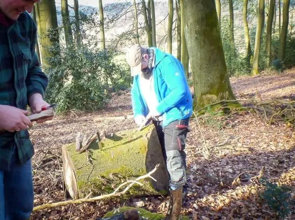 Messer bearbeitet Holzstück auf einem moosbedeckten Baumstumpf im Wald